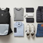 Flat lay of a minimalist travel packing list: backpack, core clothing, and essentials for carry-on only travel