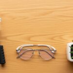 Flat lay of affordable desk accessories: sand timer, hand gripper, blue-light glasses, and a plant